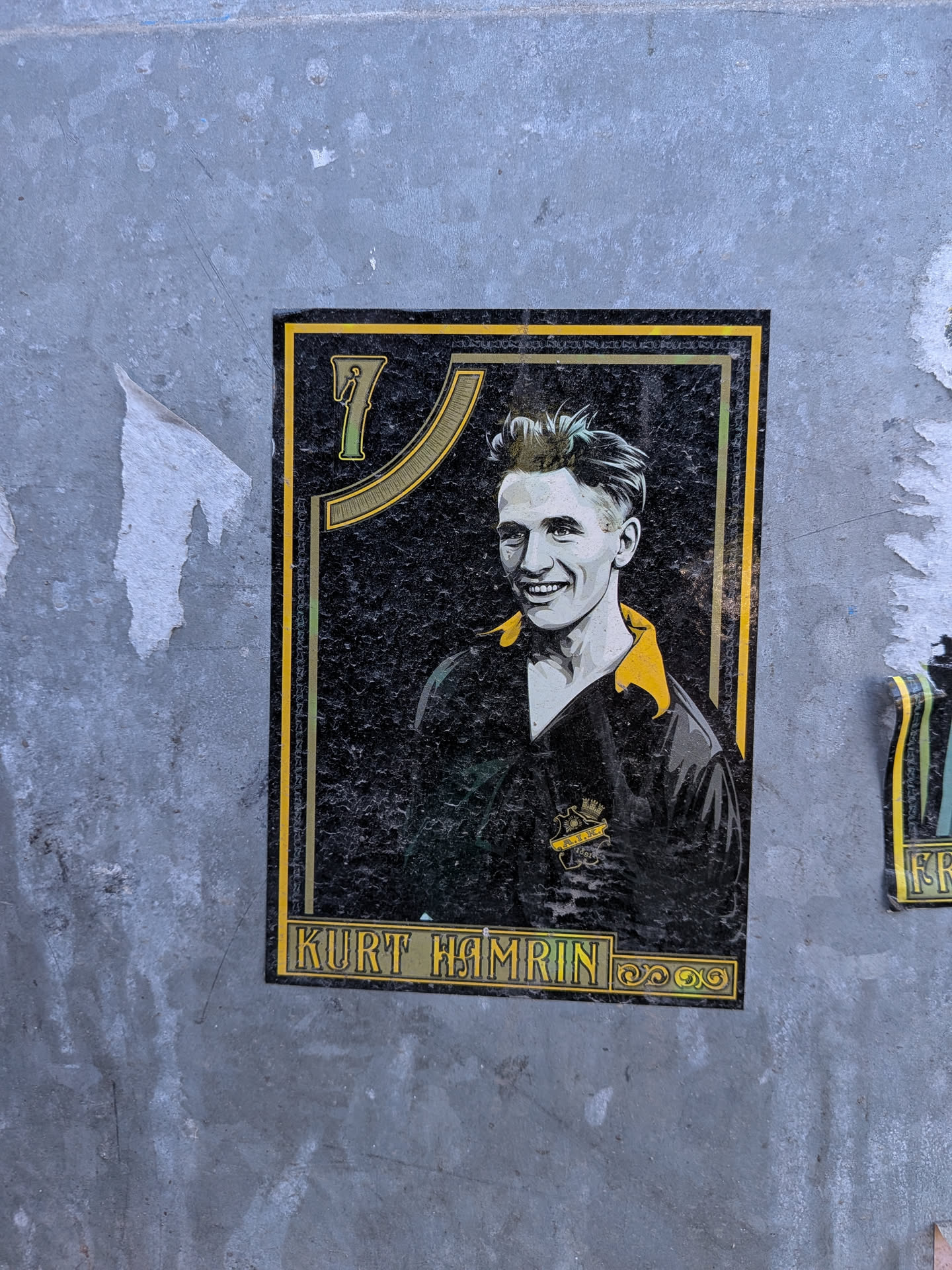 The sticker is a rectangular, vertically oriented design featuring a stylized portrait of a smiling young man, identified as Kurt Hamrin. He has short, light-colored hair and is wearing a dark shirt with a yellow collar and a crest on the left chest that reads 'A.I.K. 1891' with a crown. The background is predominantly black with a textured appearance. In the upper left corner, a prominent number '7' is displayed in green and gold, framed by a decorative golden arch. The entire portrait is bordered by a double frame of yellow/gold lines. Below the portrait, a golden banner contains the name 'KURT HAMRIN' in capital letters, flanked by decorative golden swirls. The overall style evokes a vintage sports card or commemorative artwork.