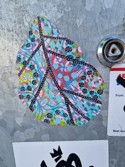 This sticker features an abstract design resembling a leaf.  It's predominantly pink, teal, and black, with various patterns and dots. The lines and shapes create a visually interesting and organic feel.