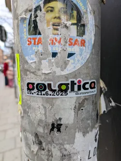 Street sticker This is a sticker advertising the Solstice Festival which will occur from June 19th to June 21st, 2025. The sticker is on a white background with a black border and features colorful circles within the word Solstice. It is attached to a light grey pole with various other stickers and posters.