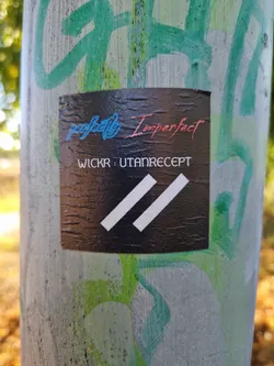 Black sticker with the text "perfectly Imperfect" in a stylized font and the Wickr contact information: "WICKR: UTANRECEPT".  It also features two parallel white stripes at the bottom. The sticker appears to be affixed to a pole with some graffiti in the background.