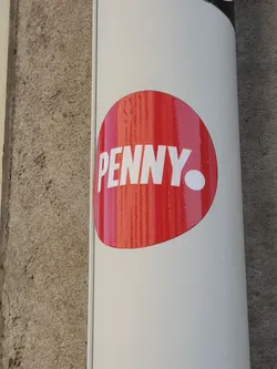 Street sticker A red circular sticker with the word "PENNY" in white text.  The sticker is affixed to a light beige cylindrical surface, possibly a pole or pipe.
