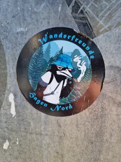 Street sticker A round sticker featuring a cartoon bird wearing a bucket hat and smoking a pipe. The bird is set against a backdrop of mountains and trees. The text "Wanderfreunde" and "Sagen Nord" is written around the bird.