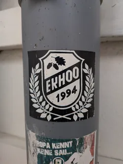 Street sticker A square black sticker displaying a white shield emblem. The shield contains an oak leaf with acorns, the text 'EKHOO' on a diagonal band, and the year '1994'. A white laurel wreath surrounds the shield.