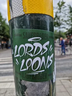 Street sticker A green sticker with white graffiti-style lettering reading "LORDS\' LOONS" with the words SAUERBRÜDER and RAUBBRÜDER on the top and bottom in a smaller font.  There's a small halo-like symbol above the main text.