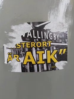 Street sticker A sticker featuring a black and white image of a street scene with yellow text overlay that reads "VALLINGBY ÄR AIK". The text "VALLINGBY" is on top and smaller. The text "ÄR AIK" is larger and bolder, with the letters AIK being very prominent.  The sticker appears to be weathered or torn at the edges.