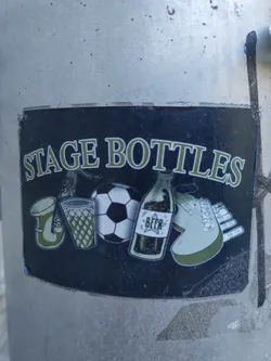 A sticker depicting various items associated with a stage or performance, including a beer bottle, soccer ball, musical instrument, and glass.  The style is illustrative and slightly vintage.