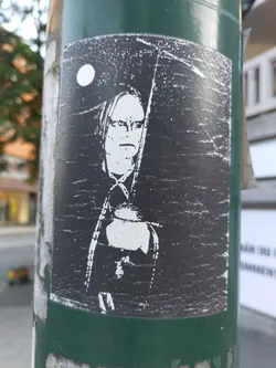 A black and white sticker depicting a person with long hair, possibly a grim reaper, standing under a full moon. The style is dark and mysterious, with a distressed look to the sticker itself, adding to its grungy aesthetic.