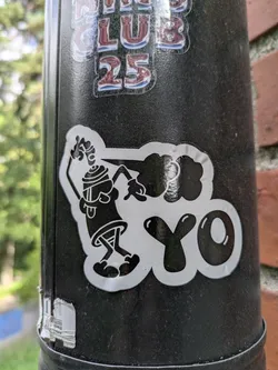 Street sticker The sticker features a black and white cartoon illustration of a spray paint can character in a dynamic pose. The character is shown from the chest down, with its arms extended. It appears to be actively spraying, with a cloud-like shape emanating from the nozzle. The cloud is stylized and forms the word "YO". The character itself has a distinct silhouette, with legs bent and feet pointing outwards. The overall style is reminiscent of graffiti art and urban culture.