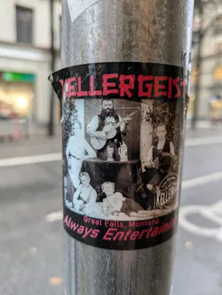 Street sticker A sticker featuring a black and white photo of a band, possibly called Kellergeist, from Great Falls, Montana. The photo shows a man playing a guitar and other people surrounding him.  The text "Always Entertaining" is written below the photo.
