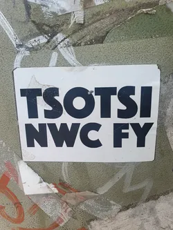 Street sticker A white sticker with black bold text that says TSOTSI NWC FY is stuck on a wall with other graffiti. The sticker is slightly damaged on the edges.