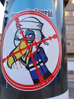 Street sticker The sticker depicts a cartoon toucan in a sailor's hat, seemingly targeted by a crosshair. It has a dark and slightly morbid aesthetic.  The background is partially visible and seems to show another sticker.