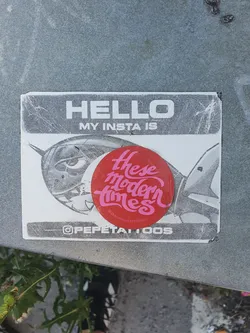 A sticker featuring a red circle with the text "These Modern Times" in a pink script font.  The sticker is part of a larger design including a drawing of a rocket or plane and text that reads "HELLO MY INSTA IS" and "@PEPETATTOOS".
