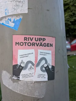 Street sticker The sticker features a pink background with the text "RIV UPP MOTORVÄGEN" in large, bold black letters at the top. Below this, two torn pieces of paper are depicted, each with a road winding through miniature cityscapes. The left piece has text that reads "TVÄRFÖRBINDELSE SÖDERTÖRN*" and below that "*INNEHÅLLER SPÅR AV GRÖNMÅLNING OCH FOSSILKAPITALISM". The right piece reads "TRAFIKVERKETS VÄGPLAN**" and below that "**FRAMTAGEN I SAMRÅD MED OKQ8 OCH BMW". Two black, stylized hands are shown holding and tearing the two pieces of paper apart, illustrating the message of dismantling the highway. The overall aesthetic is somewhat rough and distressed, with subtle speckling on the pink background.