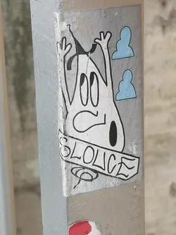 Street sticker The sticker features a stylized, somewhat amorphous white character with a thick black outline, resembling a ghost or a blob-like figure. It has large, oval-shaped eyes looking upwards and a small, downturned mouth, conveying a surprised or distressed expression. Two arms are raised with three-fingered hands. A small black tear-drop shape is visible on its lower right side. To the right of the character, there are two light blue, cloud-like or abstract head-like shapes, also with black outlines. Below the character, a banner-like element contains the text "SLOLICE" in bold, blocky, black capital letters. The sticker itself has a light grey background and shows significant signs of wear, cracking, and peeling, indicating its age and exposure to elements. A faint, light brown '18' is barely visible above the character's head.