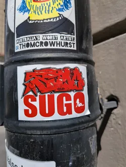 Street sticker White rectangular sticker featuring a red graffiti-style tag above the word 'SUGO' in bold red block letters. The 'O' contains a white silhouette of a reclining woman.