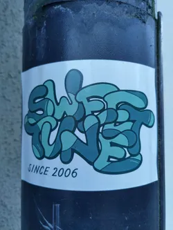 Street sticker A sticker with the words "Sweet Tune" in stylized lettering. The text "Since 2006" is written underneath the main text. The style is reminiscent of graffiti art, with bubble letters in shades of teal and dark green.
