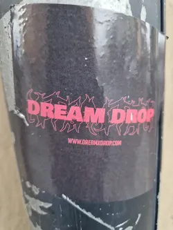 A black sticker with the text DREAM DROP in pink.  There is a website address at the bottom. The text is stylized with figures surrounding it.