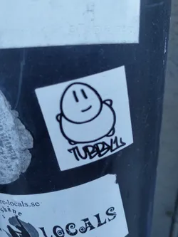 Street sticker A white square sticker with a simple black line drawing of a chubby, smiling character. The name "TUBBY" is written underneath in graffiti style.