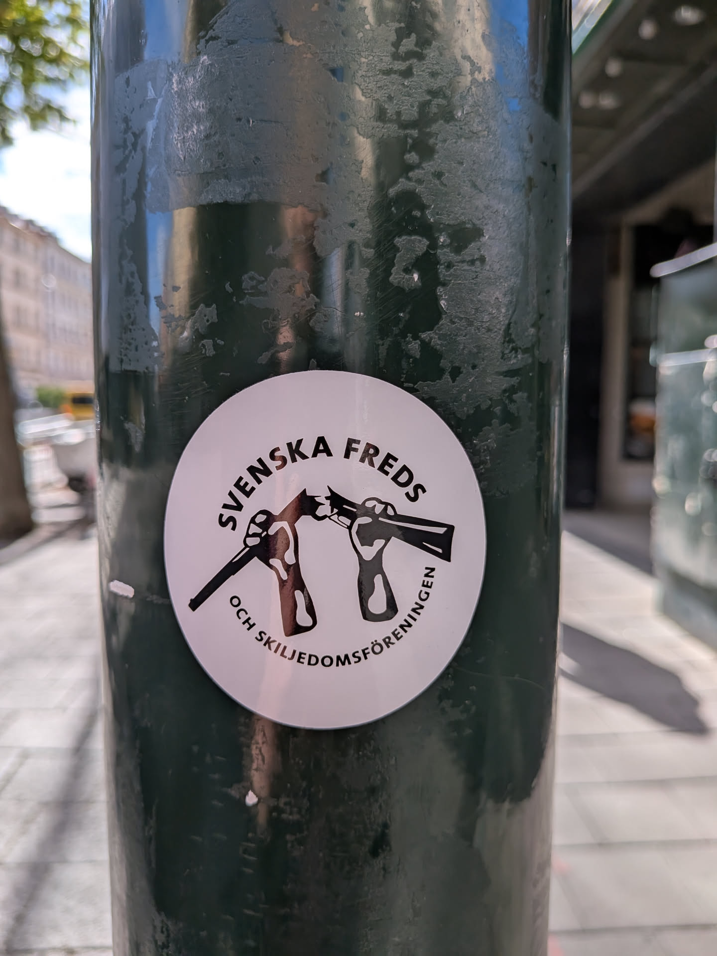 A circular white sticker featuring a black graphic of two hands breaking a rifle in half. The Swedish text 'SVENSKA FREDS OCH SKILJEDOMSFÖRENINGEN' is printed in black, curving along the top and bottom borders.