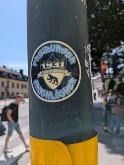 Street sticker A round black sticker featuring a central gold and black shield with the Bern bear, the year '1931', and a banner reading 'SZENE BERN'. Curved light-blue text reads 'FREIBURGER' at the top and 'ARSCHLÖCHER' at the bottom.