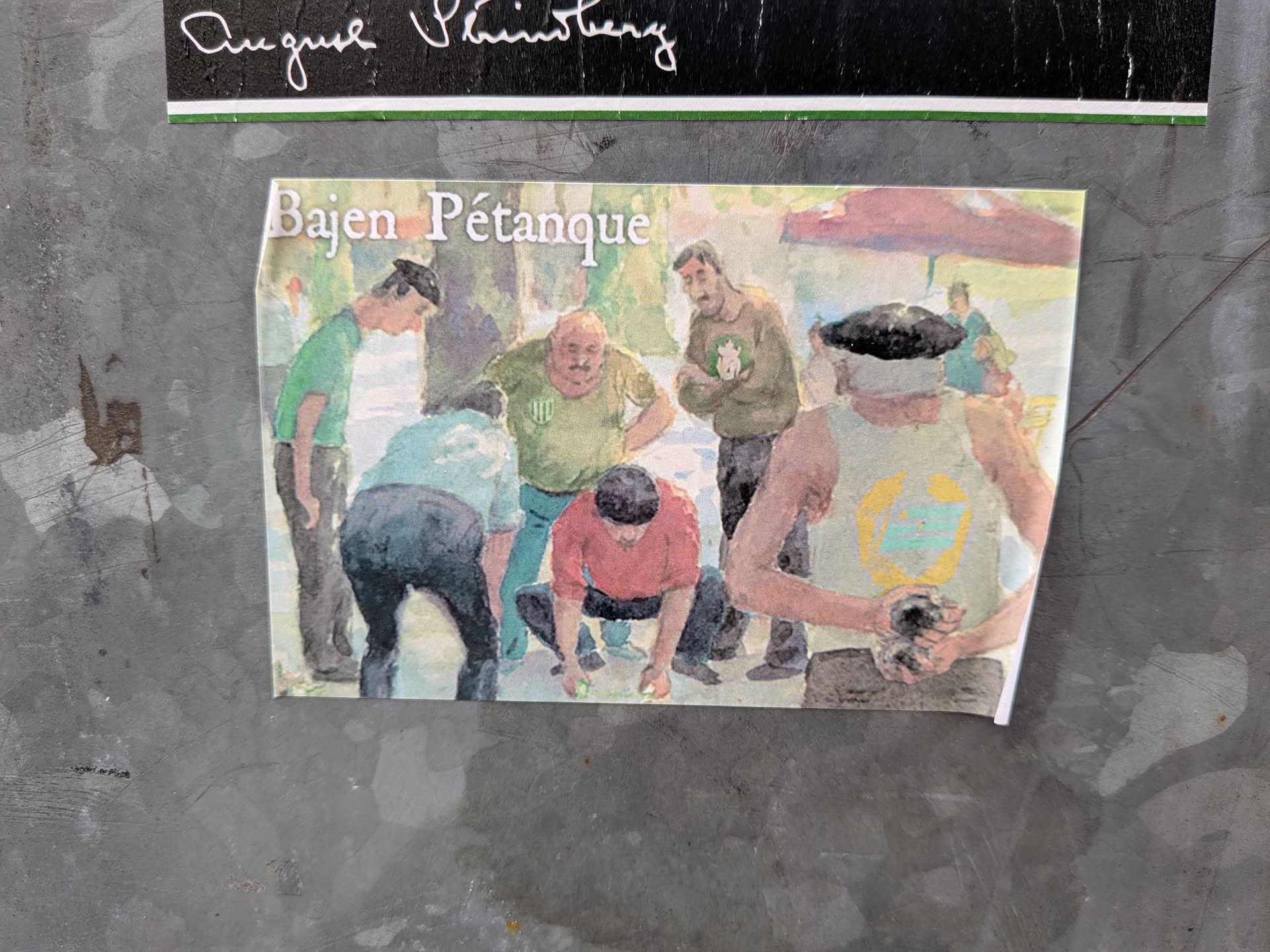 A rectangular sticker featuring a watercolor-style painting of a group of men playing pétanque outdoors. The text 'Bajen Pétanque' is printed in white serif font at the top left. The scene depicts several men in casual clothing, some wearing green and white colors associated with the Swedish club Hammarby ('Bajen'). One man in a red shirt is crouching to measure or play, while others watch intently. In the foreground, a man wearing a dark beret and a light green tank top holds a pétanque ball. The background shows a park-like setting with trees and a red parasol.