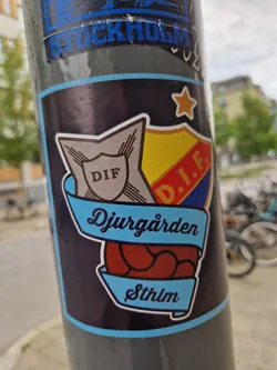 Street sticker A sticker featuring the logo of Djurgårdens IF, a football club from Stockholm, Sweden. The logo is a shield with the club's initials and a stylized soccer ball. The text 'Djurgården' and 'Sthlm' are prominently displayed.