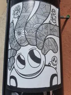 Street sticker This sticker showcases a charming character with a complex, textured hairstyle composed of various lines and patterns. Smaller versions of the character are visible on either side, adding to the playful aesthetic. The entire design is executed in black and white, emphasizing the details and creating a visually engaging piece. 