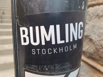 A black and white sticker with the text "BUMLING STOCKHOLM" on it. The sticker is slightly damaged.