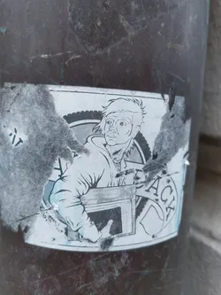 The sticker shows a stylized drawing of an individual, seemingly carrying or placing a box into something resembling a fireplace or oven. The style is minimalistic, using shades of gray and white.  The sticker itself is damaged and torn at the edges.