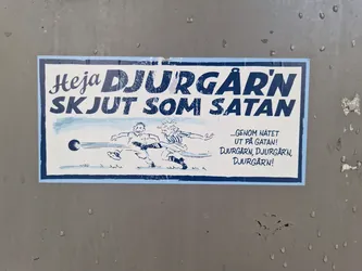 A sticker featuring a cartoon illustration of people playing a sport, with text in Swedish. The text translates to something like 'Go Djurgården! Shoot like Satan!' with a secondary slogan suggesting a celebration in the streets.