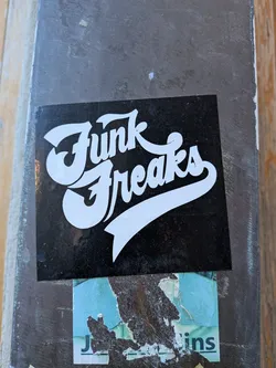 Street sticker A rectangular sticker with a solid black background. The words "Funk Freaks" are prominently displayed in white, using a bold, stylized script font with a retro aesthetic. The letters are thick and rounded, with a slight shadow effect. The word "Funk" is positioned above "Freaks," and both words feature elongated, swooping tails, particularly from the 'k' in "Funk" and the 's' in "Freaks," giving the design a dynamic, almost calligraphic flow. The overall appearance is clean, high-contrast, and eye-catching.