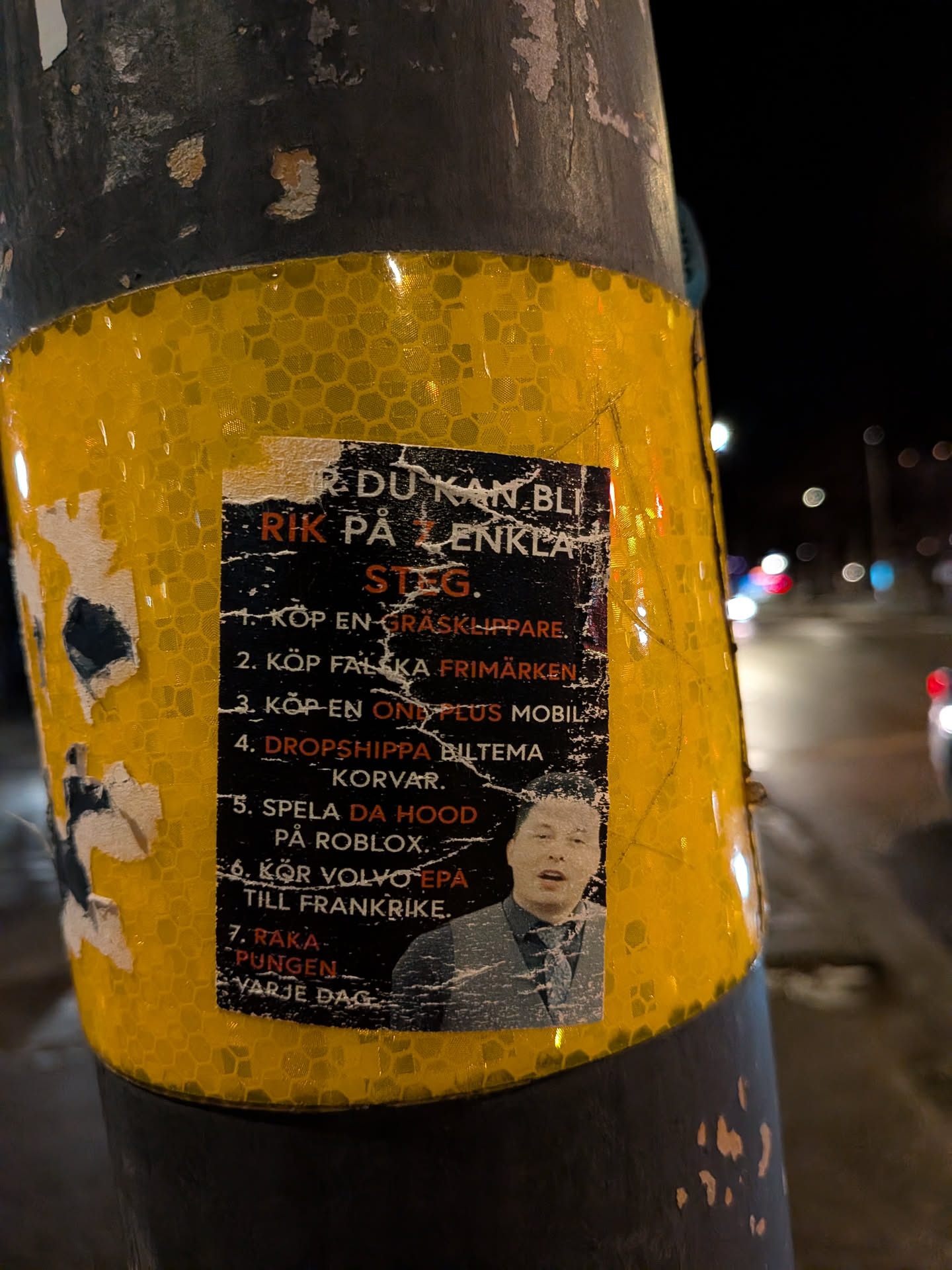 A rectangular sticker with a black background and white text, featuring a numbered list of 'easy steps' to become rich. At the bottom right, there's a color photo of a young man with an open mouth, wearing a collared shirt, patterned tie, and a grey vest. The sticker shows signs of wear, with white scuffs and peeling, particularly along the edges and over the black background. It is affixed to a yellow reflective pole with a honeycomb pattern, which is also partially covered in a dark, possibly black, material.