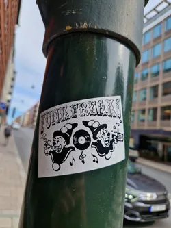 Street sticker A black and white sticker featuring two clown-like characters with a vinyl record, musical notes, and what seems to be a cassette tape or similar object. The text "Funk Freaks" is prominently displayed at the top. The style is reminiscent of vintage or retro designs.