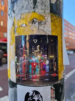 Street sticker A sticker depicting a blurry night scene of a city street with bright lights and reflections in the wet pavement. The style is impressionistic and captures the atmosphere of a bustling city at night.  There is a small, indistinct symbol near the center of the image.