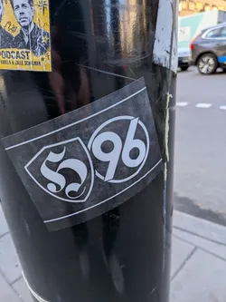 Street sticker A rectangular sticker with a dark, textured grey background. On the left, a white shield outline encloses a stylized gothic blackletter 'S'. On the right, a white circle encloses the number '96' in a bold, sans-serif font, representing the Hannover 96 football club logo. The sticker has thin white border lines along the top and bottom.