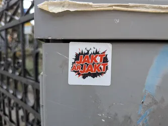 Street sticker Square white sticker featuring bold red text "JAKT ÄR JAKT" over a black splash background containing silhouettes of a stag, pine trees, and a bird.