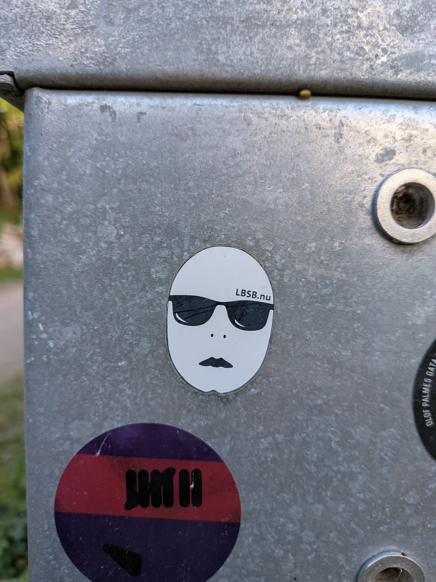An oval white sticker featuring a simple face graphic with black sunglasses, two small dots for nostrils, a stylized mouth, and the text 'LBSB.nu' printed above the right lens.