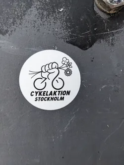 A black and white sticker with a drawing of a fist holding flowers and bicycle wheels. The text "Cykelaktion Stockholm" is written below the drawing.