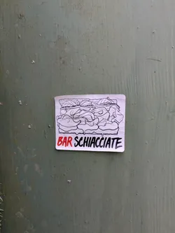 Street sticker This sticker features a hand-drawn illustration of a schiacciata sandwich with ingredients spilling out. The words "BAR SCHIACCIATE" are printed in red underneath the sandwich. The sticker is adhered to a green background. The artwork has a homemade feel, hinting at a local business.