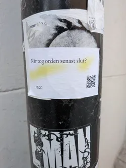 The sticker is a rectangular piece of white paper, slightly creased and textured, adhered to a dark, textured pole. It features black text in a sans-serif font. The main text, "När tog orden senast slut?", is centrally located and has a subtle, uneven yellow highlight underneath it. Below this, in the bottom left corner, are the numbers "12/20". In the bottom right corner, there is a clear, black and white QR code. The sticker appears to be placed over other older, torn stickers or papers, showing signs of wear and outdoor exposure.