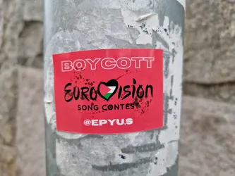 Street sticker A red sticker with white and gray text expressing a boycott of the Eurovision Song Contest.  The sticker includes a heart incorporating the Palestinian flag. 