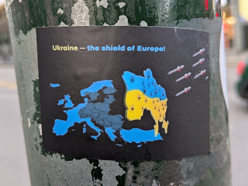 Street sticker A sticker depicting a map of Europe with Ukraine highlighted in the colors of the Ukrainian flag. Missiles are shown flying towards Ukraine. The text on the sticker reads "Ukraine - the shield of Europe!"