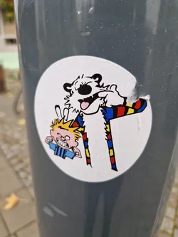 This round sticker showcases a dynamic scene from the Peanuts comic strip.  It features Charlie Brown and Snoopy in a humorous interaction. The art style is consistent with the original comic, using simple lines and bold colors. The sticker is slightly damaged along one edge, showing signs of wear.