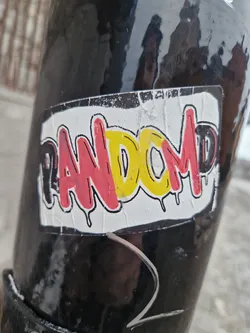A sticker with the word "RANDOM" written in graffiti-style lettering. The letters are in red, yellow, and black with dripping paint effects. The sticker is slightly worn and peeling at the edges.