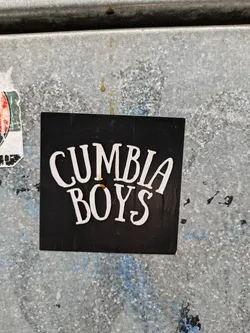 Street sticker A black sticker with the text "Cumbia Boys" in white stylized lettering. The sticker is affixed to a weathered metal surface.
