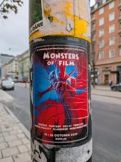 Street sticker The sticker is a poster for the 'Monsters of Film' event, part of the 14th Stockholm International Fantastic Film Festival. It features a striking, abstract illustration of a creature with multiple tentacles and a central eye-like feature, rendered in vibrant blues and reds. The background is a chaotic blend of these colors, suggesting a dynamic and possibly unsettling theme. The text is in white and is arranged in a structured manner, with the festival name and dates clearly visible. The overall aesthetic is bold and eye-catching, typical of promotional material for a genre film festival.