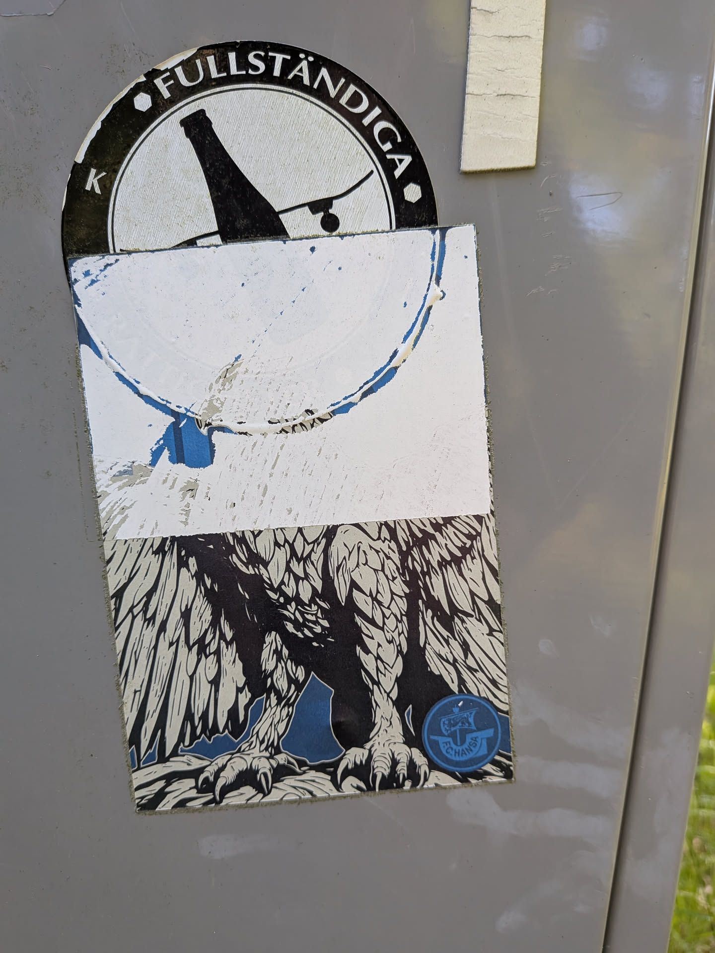 A rectangular sticker, heavily peeled and damaged at the top. The lower portion displays a detailed black-and-white illustration of a griffin's legs and wings on a blue background. A small blue circular FC Hansa Rostock logo is visible in the bottom right corner.