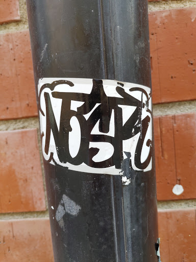 A close-up shot of a black and white sticker on a dark-colored pipe. The sticker features graffiti-style lettering, which appears to say "NDSPZ". The sticker is slightly worn and peeling at the edges.