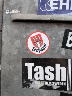 Street sticker A circular sticker featuring a bold red outer border and a clean white background. The upper half displays a red shield containing a white depiction of a castle with three towers, a central gate, and a star positioned above the middle tower. Below this emblematic crest, the words "St. Pauli" are written in a distinctive, flowing black script.