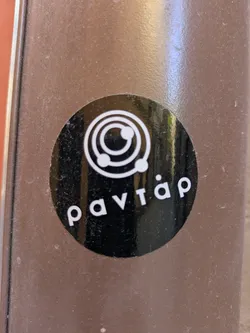 Street sticker The sticker is a black circle with white text and an icon. The text reads 'pavtar'. Above the text, there is a circular icon with three smaller circles around a central circle, resembling an atom or a planetary system.